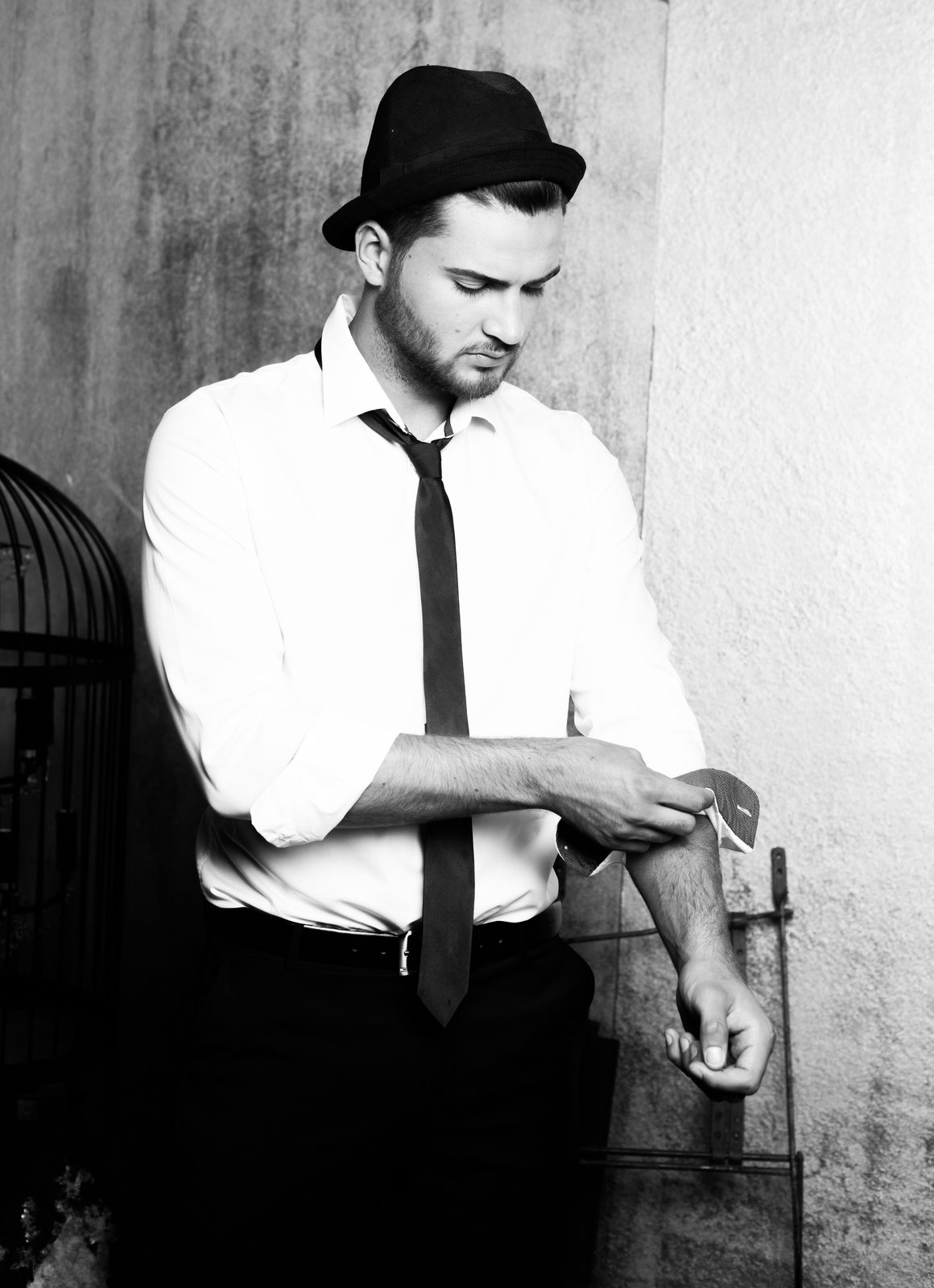 Man in hat and tie rolling up his shirt sleeve — black and white portrait