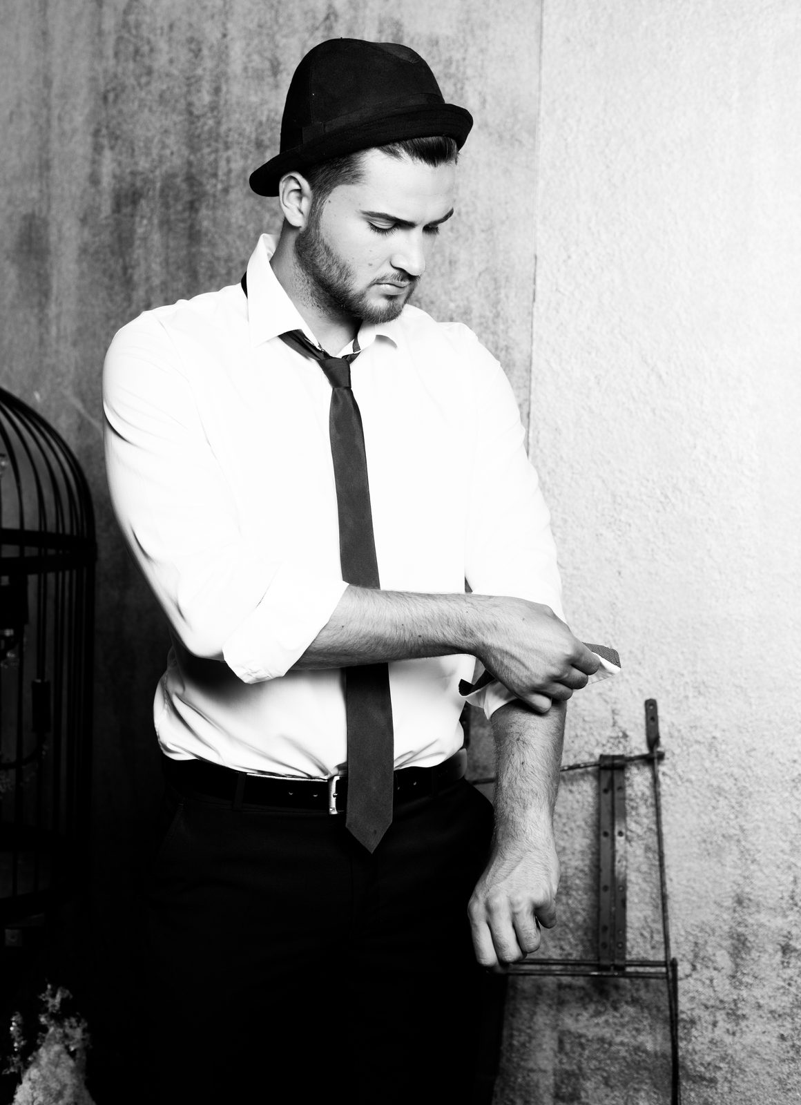 Man in hat and tie rolling up his shirt sleeve – black-and-white portrait