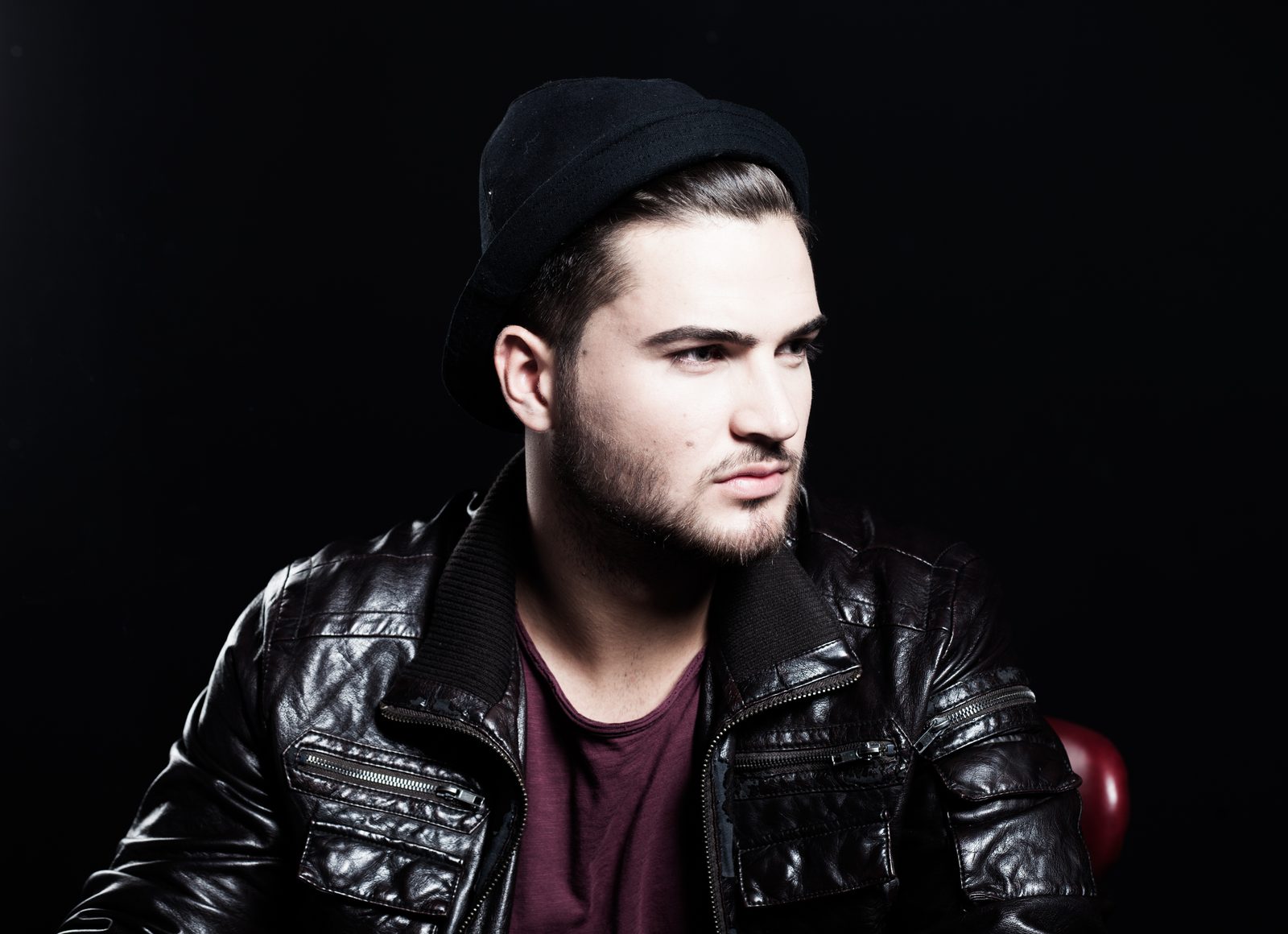 man in beanie and leather jacket against a dark studio background