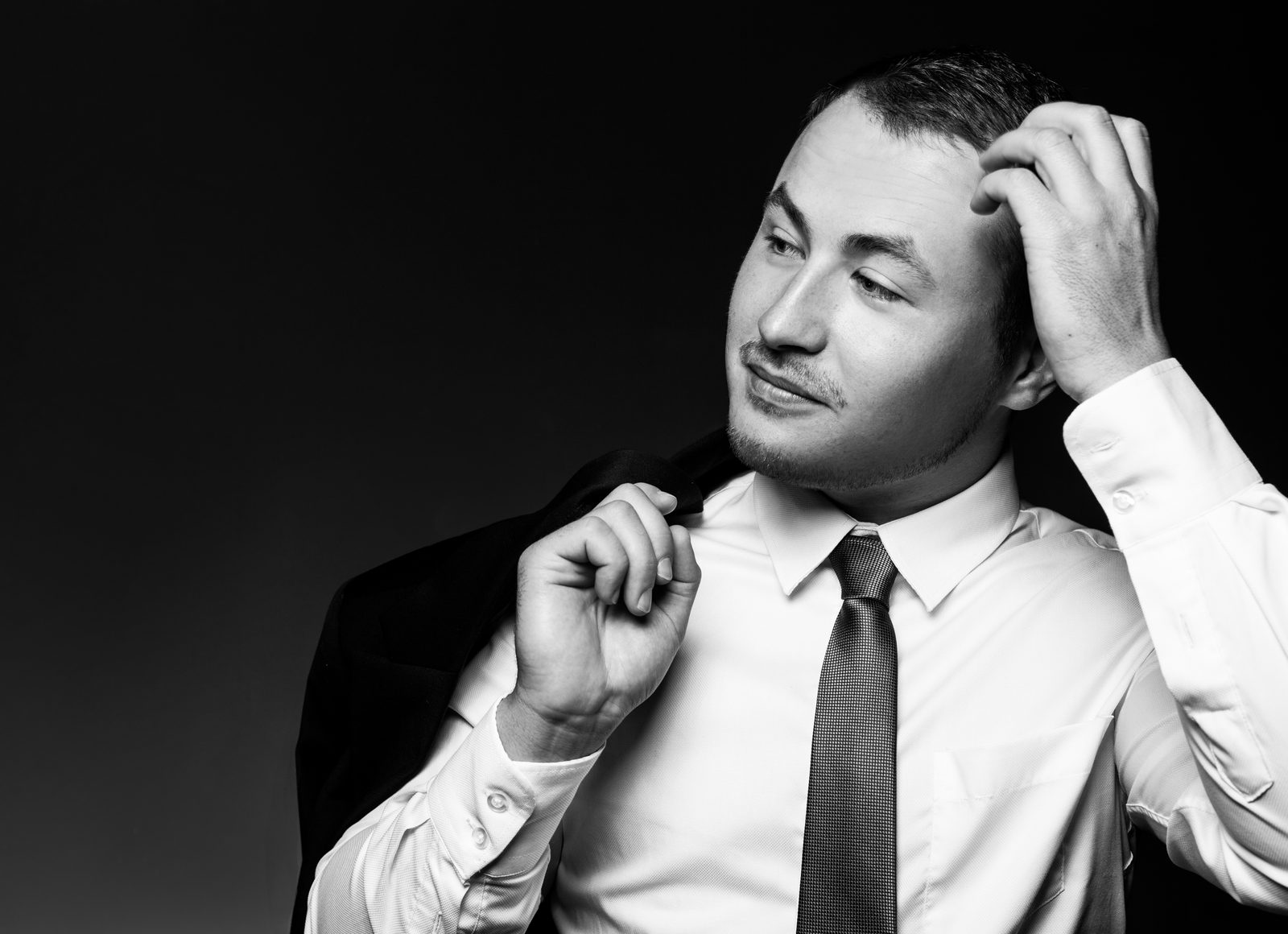 Man in white shirt and tie holds jacket over his shoulder—studio portrait in Hamburg