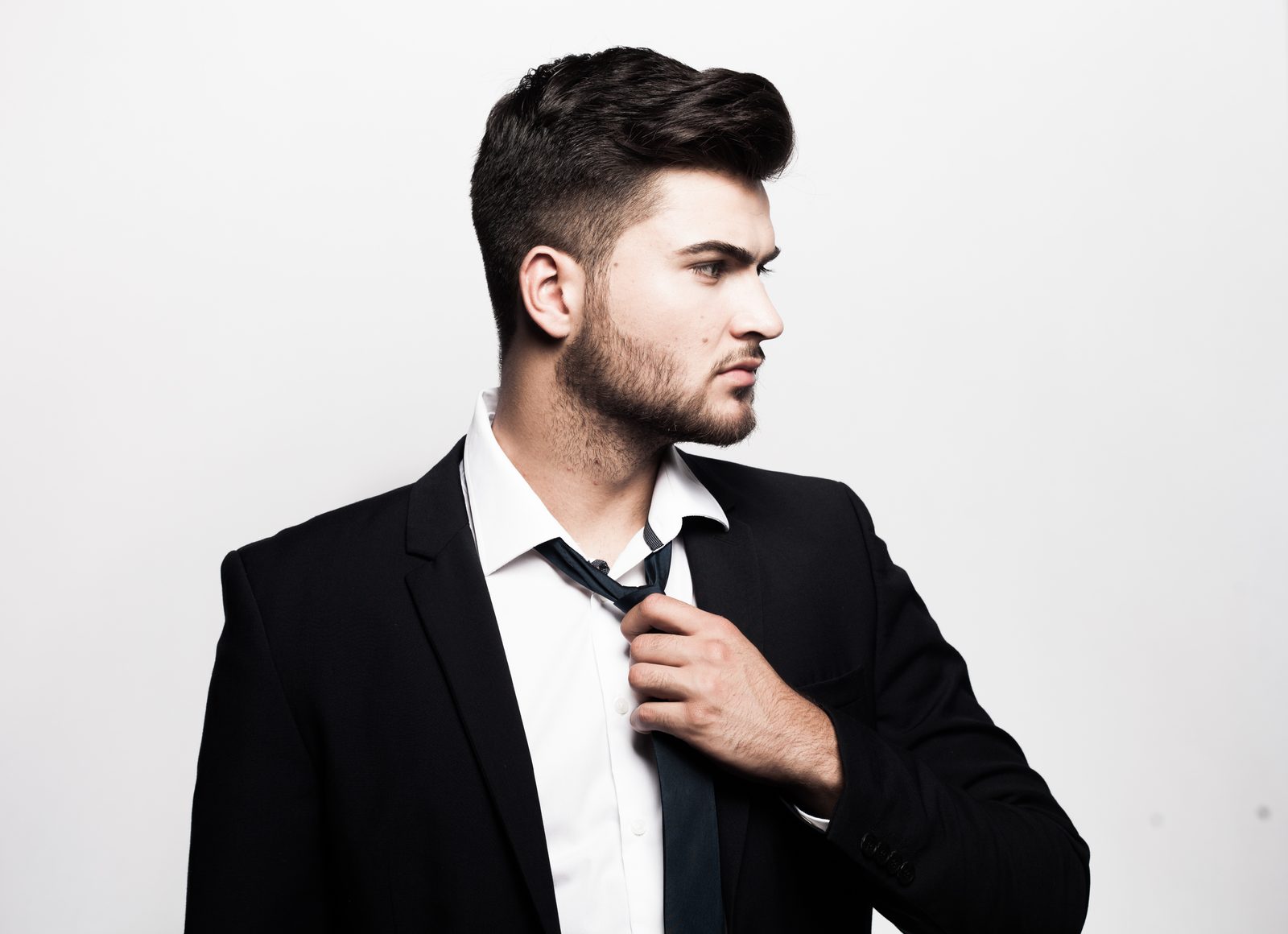 Man in a suit adjusting his tie in a bright studio setting