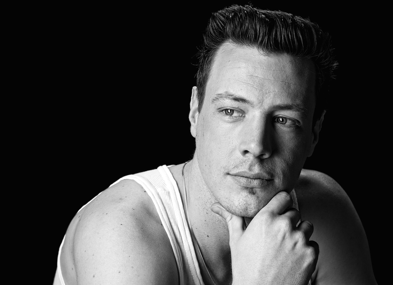 Black-and-white portrait of a man resting his chin on his hand against a dark background