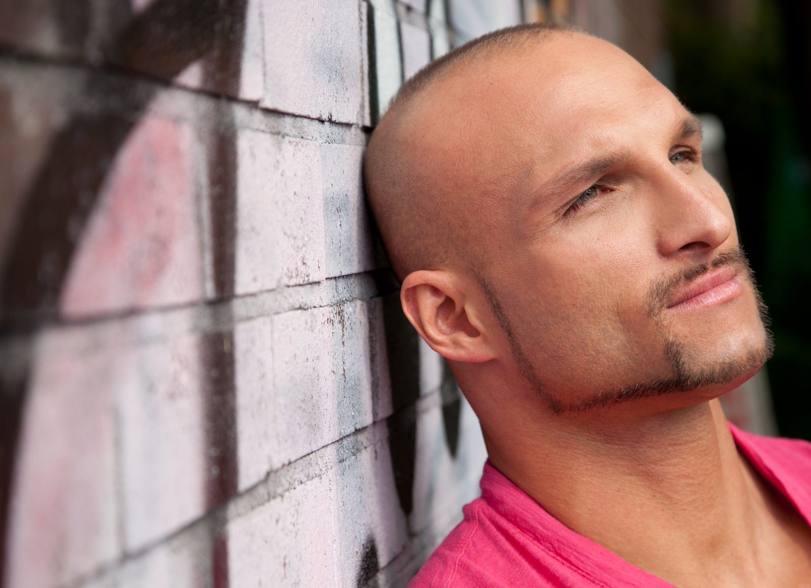 bald man leans head against painted brick wall—outdoor portrait