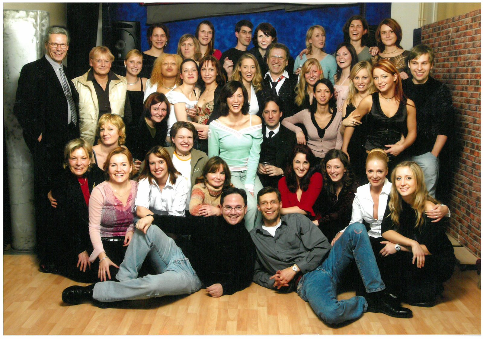 Große Gruppe lachender Menschen posiert für ein Teamfoto im Studio